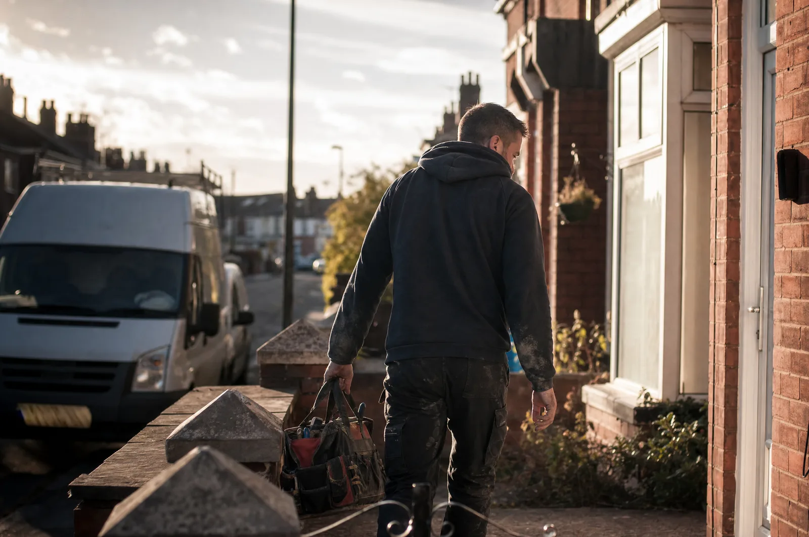 Tradesperson arriving at a UK terraced house, work van parked behind them